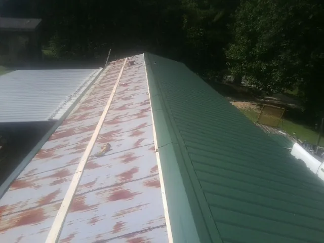 Old rusted panels beside newly installed green metal roofing — Wind Damage Roof Repair by Roofing Brothers in Hollister