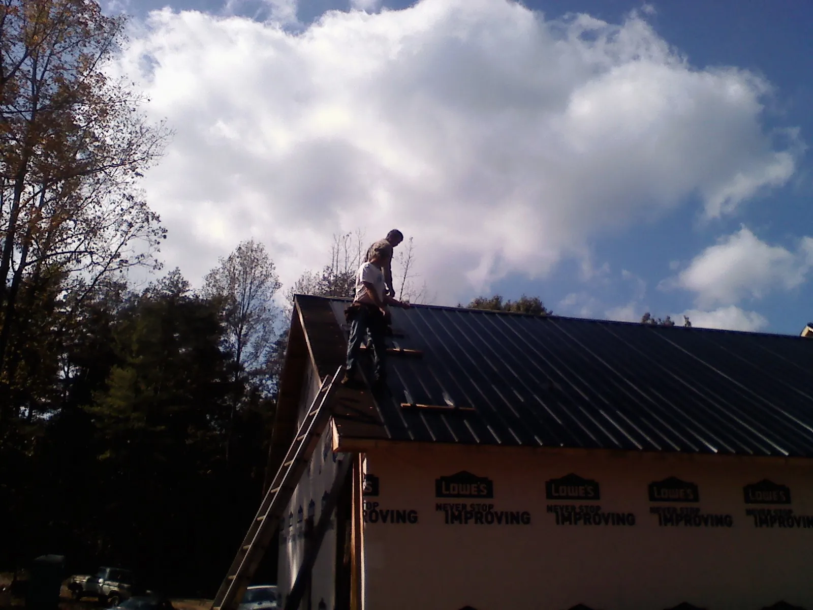 Roofer fastening dark metal panels high against a cloudy sky, from a Roof Inspection job in Hollister